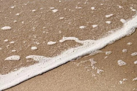 Foamy ocean wave sliding across sandy beach under soft daylight Stock Photos