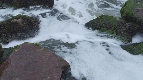 Foamy ocean waves crushing about algae covered rock boulders Stock Footage 160887783