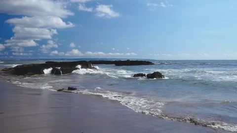 Foamy ocean waves washing dark sand beach with rocks Stock Footage 82806842