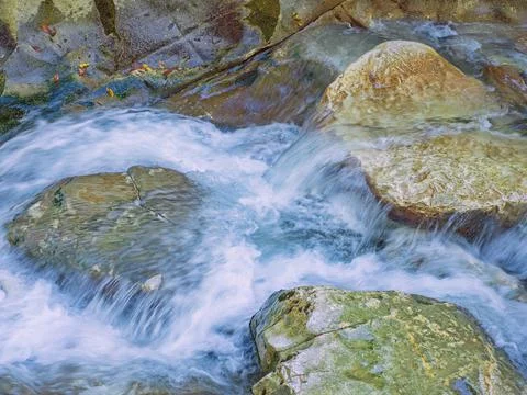 A foamy river with clear water flows over large stones. Closeup photo Stock Photos