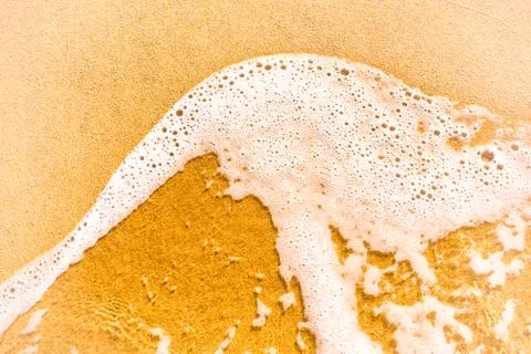 Foamy wave on sandy beach. Stock Photos