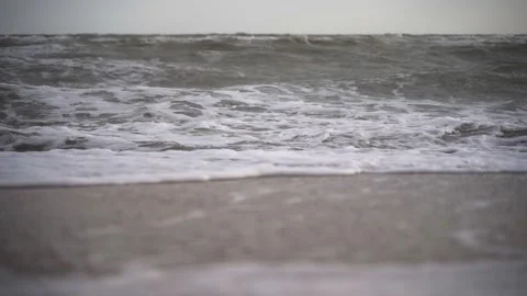 Foamy waves crash onto sandy shore. Dynamic ocean scenery with natural light Stock Footage 258799495