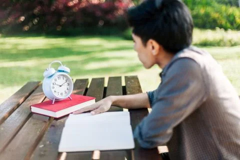 Focus on clock, Young man looking at clock while studying Stock Photos