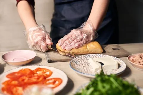 Focus on cutting with knife bread roll on cutting board for preparing panin.. Stock Photos