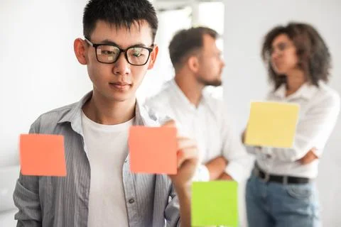 Focus ethnic guy taking notes on memo stickers during brainstorm with coworkers Stock Photos