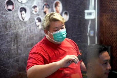 Focus on the face of a barber using mask while combing the hair of a client Stock Photos