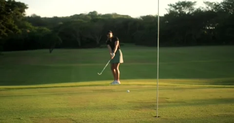 Focus on a golf hole in the background, out of focus a female golfer to hit ball 스톡 동영상 276935656