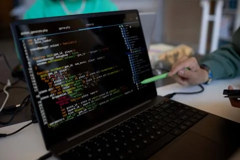 Focus on laptop screen with coded data and pen held by hand of young man Stock Photos
