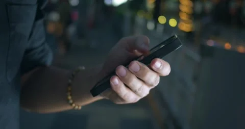 Focus on male hand using mobile phone at night city street background. Close up Stock Footage 312502214