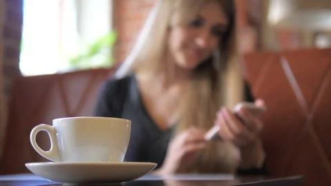 Focus on the mug, a woman using a smartphone in the background is blurred. Stock Footage 79403673