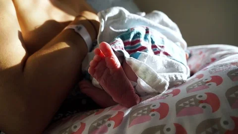 Focus on newborn baby's foot as she nurses in her mother's arms in the hospital Stock Footage 83057510