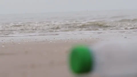 Focus Pull from Small Waves on Bleak Beach to Plastic Bottle Lying on Sand Stock Footage 318950560