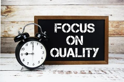 Focus On Quality text message and alarm clock on wooden background Stock Photos