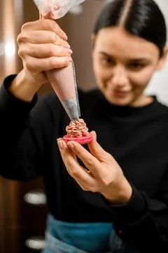 Focus on the red half of the macaroon, on which the female pastry chef applies 스톡 사진