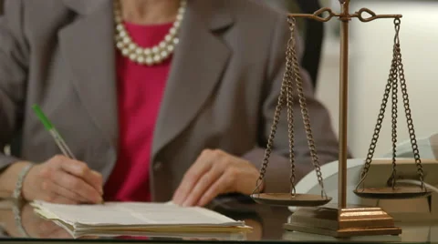 Focus on scales of justice while woman lawyer signs legal papers Stock Footage