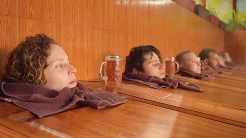 Focus shift on each head of a group of tourists relaxing on steam sauna boxes at Video stock 119801299