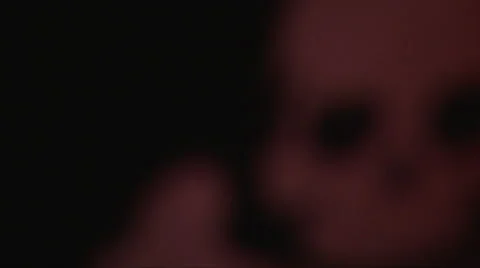 Focus shift out blur of close up hanging ruddy skull at dark background Stock Footage