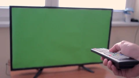Focus on TV remote control changing channels on big TV with green screen Stock Footage 93873798