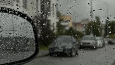 Focus on wet water drops on a vehicle window with blurred street view, cars Stock Photos
