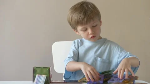 Focused 4-year-old blond boy carefully builds colorful structure with magnetic Stock Footage 318294550