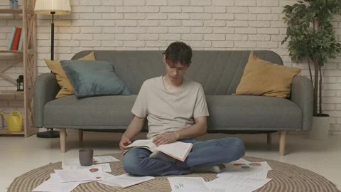 Focused adult man college student sitting on the floor in apartment room at Stock Footage 280767578