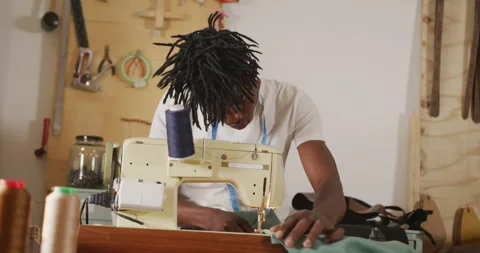 Focused african american craftsman with dreadlocks using sewing machine in Stock Footage 344324020