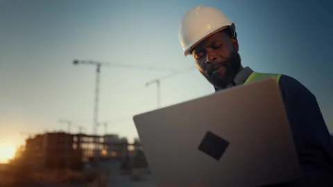 Focused african foreman looking at laptop display at construction site. Portrait Stock Footage 317806722