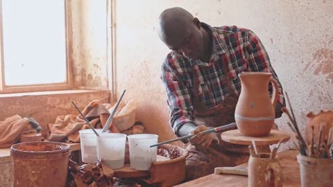 Focused African guy working in pottery workshop, painting ceramic jug he created Stock Footage 264098951