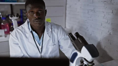 Focused african scientist analyzing samples using a microscope in a modern .. Vidéo 261370896