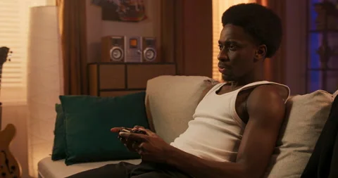 A focused afro man plays a video game on a console. A lone guy is sitting in Stockbeeldmateriaal 200806733