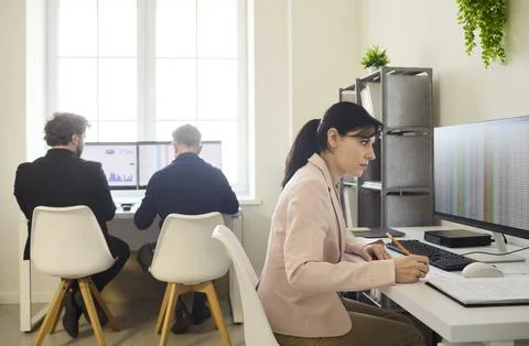Focused analyst working at computer as colleagues review charts in office Stock Photos