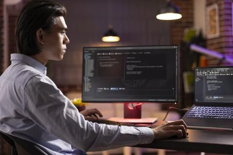 Focused asian man coding on multiple screens at home 스톡 사진