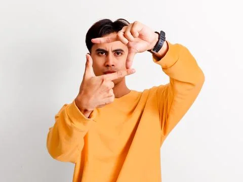 Focused Asian man making frame gesture with hands looking through fingers i.. Stock Photos
