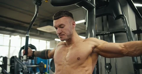 A focused athlete flexes his arm muscles on the exercise machine. Working out Video stock 241006690