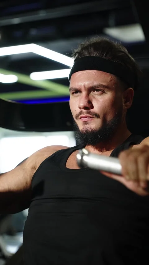 Focused athlete performing seated cable chest press in a modern gym, capturing Vidéo 329679107