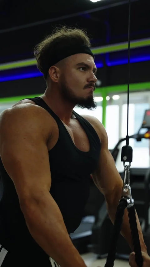 Focused athlete performs cable triceps pushdowns in a modern gym, showcasing 库存影片 329679094