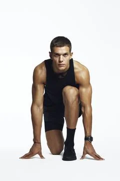 Focused athlete preparing for sprint in studio, showcasing strength and Stock Photos