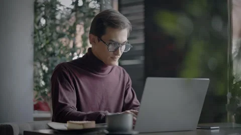 Focused attractive man with glasses typing on laptop keyboard while sitting at Stock Footage 344800237