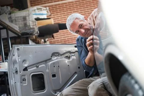 Focused auto body worker examining panel on car Stock Photos