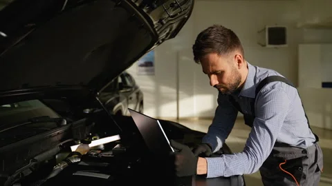 Focused auto mechanic diagnosing car engine with laptop Stock Footage 300612476