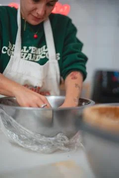 A focused baker with visible tattoos on her arm and a nose ring is actively.. Stock Photos