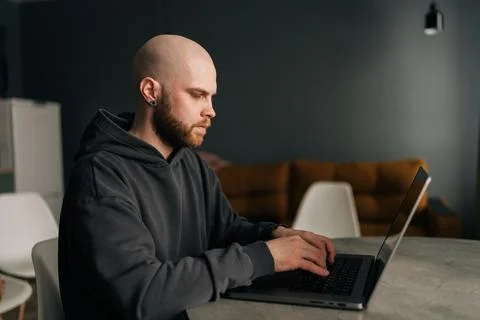 Focused bald male programmer with beard and hoodie working typing on laptop Foto stock