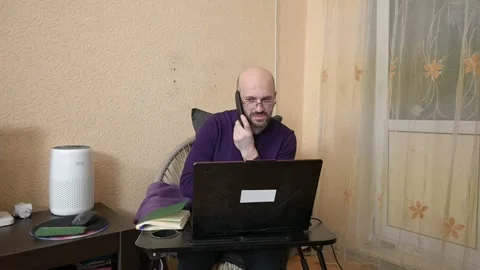 Focused bald man multitasking in his home office with a laptop and smartphone Stock Footage 329354835