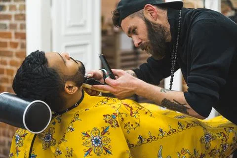Focused barber cutting client's beard in a barbershop. The process of styling a Stock Photos