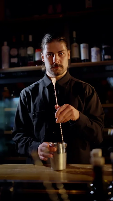 Focused bartender in a dimly lit bar stirring a cocktail with a long bar spoon Stock Footage 318541017