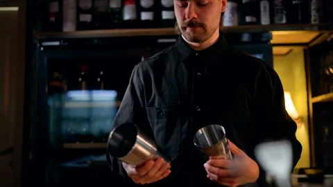 Focused bartender in a dimly lit bar prepares a cocktail with a stainless steel Video stock 318655427