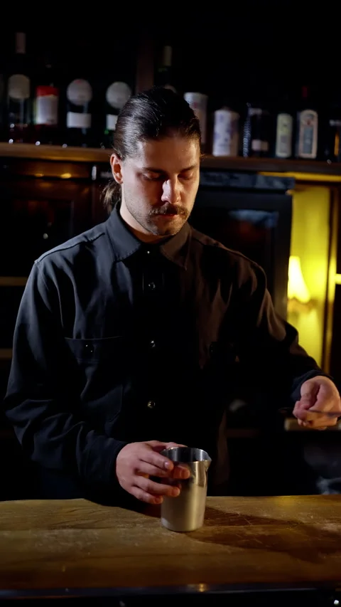 Focused bartender stirring a cocktail with a barspoon in a stainless mixing cup Video stock 318540723