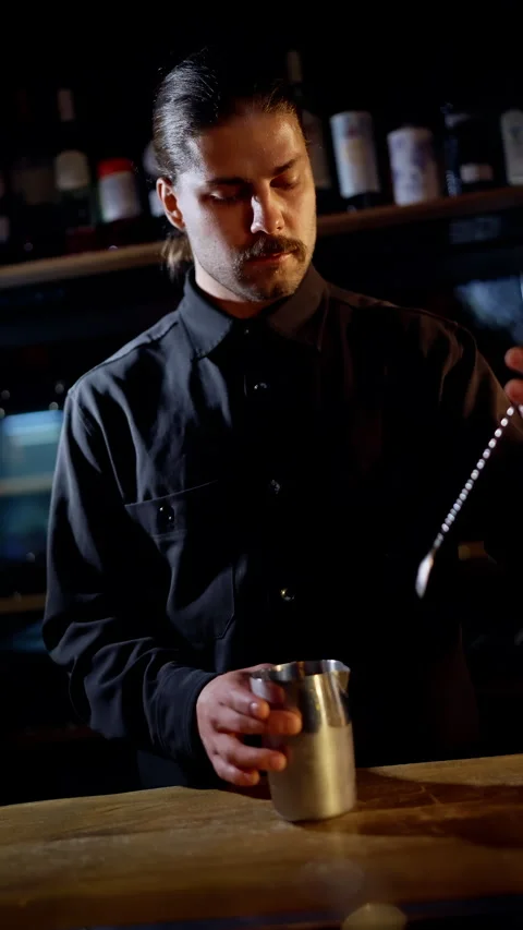 Focused bartender stirring a cocktail in a dimly lit bar, using a long bar spoon Stock Footage 318540823