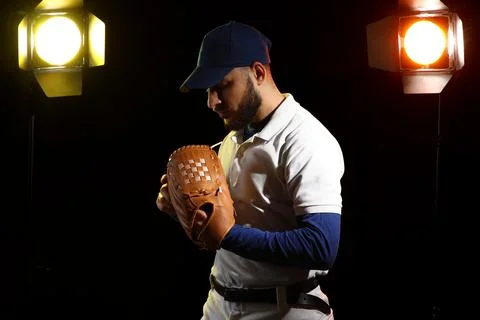 Focused baseball player in uniform holding glove under studio lights, ready f Stock Photos