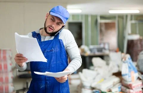 Focused bearded contractor in blue overall standing at construction site indoors Stock Photos